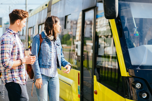 Outdoor shot of attractive millennial couple dressed casual drinks coffee from disposable cup, wanders around city, enjoys leisure time with tram on background People, transport, drinking concept. © Iryna