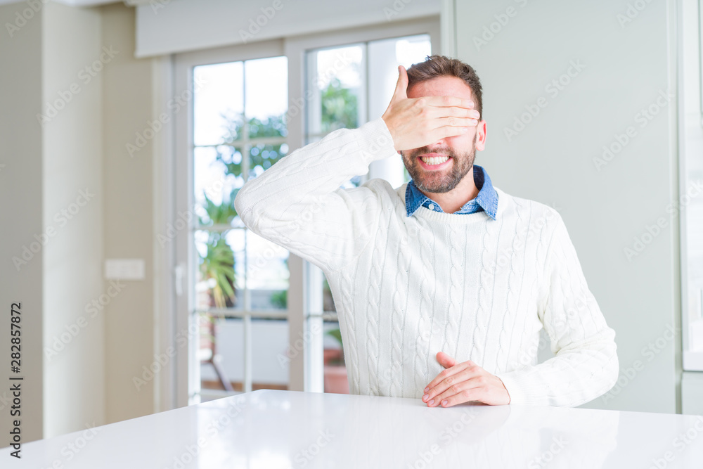 Handsome man wearing casual sweater smiling and laughing with hand on face covering eyes for surprise. Blind concept.