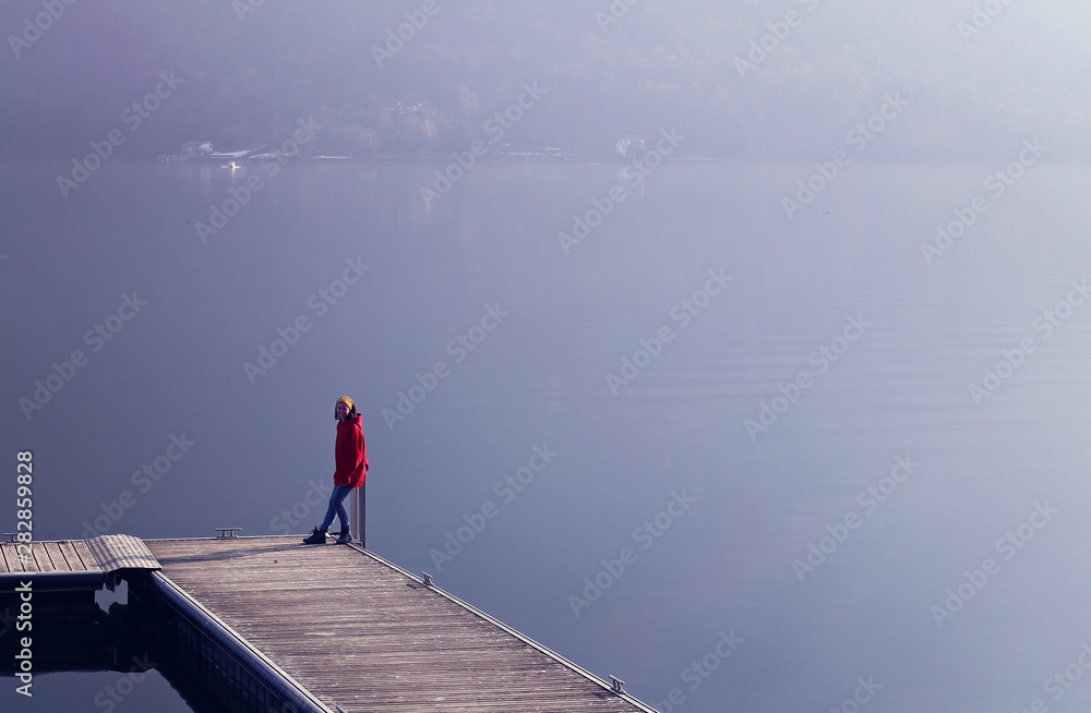 Young girl sitting on the pier on lake and mountains background.