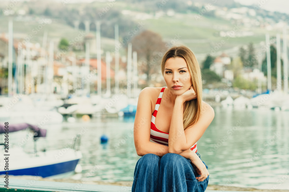 Outdoor fashion portrait of beautiful young woman posing by the lake