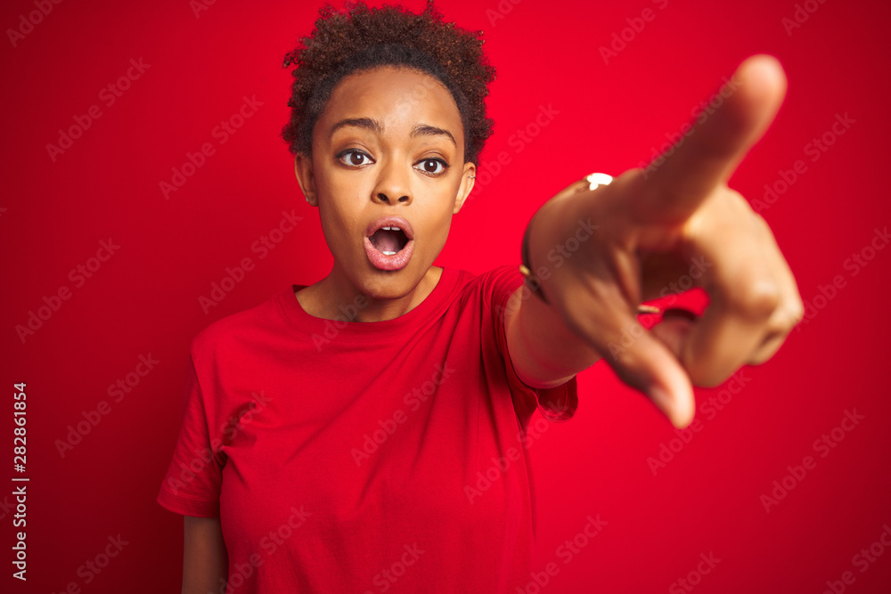 Young beautiful african american woman with afro hair over isolated red background Pointing with finger surprised ahead, open mouth amazed expression, something on the front Young beautiful african american woman with afro hair over isolated red background Pointing with finger surprised ahead, open mouth amazed expression, something on the front
