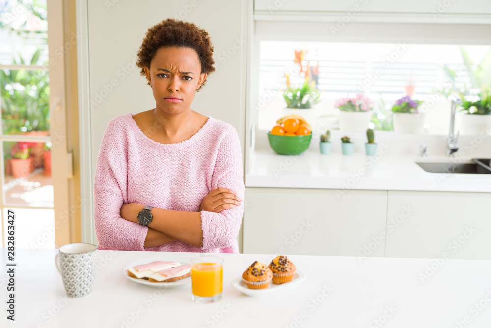 Young african american woman eating breaksfast in the morning at home skeptic and nervous, disapproving expression on face with crossed arms. Negative person. Young african american woman eating breaksfast in the morning at home skeptic and nervous, disapproving expression on face with crossed arms. Negative person.
