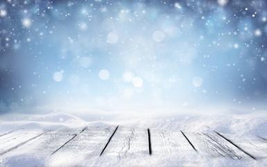 Beautiful winter snowy blurred defocused blue background and empty wooden flooring. Flakes of snow fall and sparkle on light, copy space.