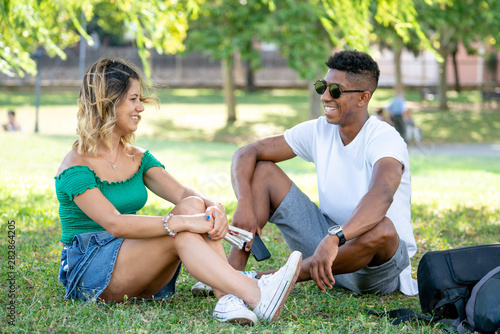 Young happy talking couple sitting under a tree on the park grass in summer