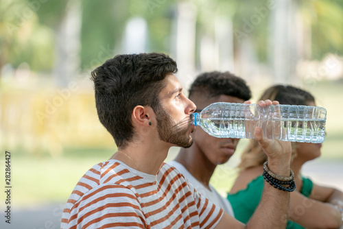 Young boy drinking water from bottle on a hot summer day in the park