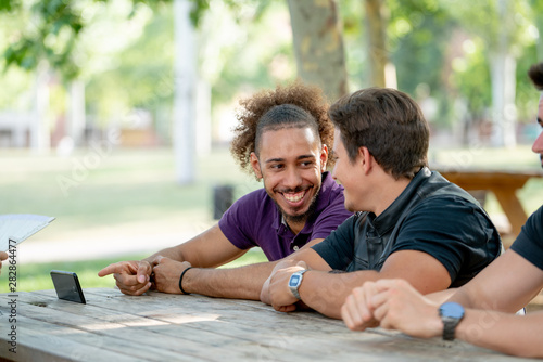 happy young men smiling and pointing at the smartphone at a park picnic table