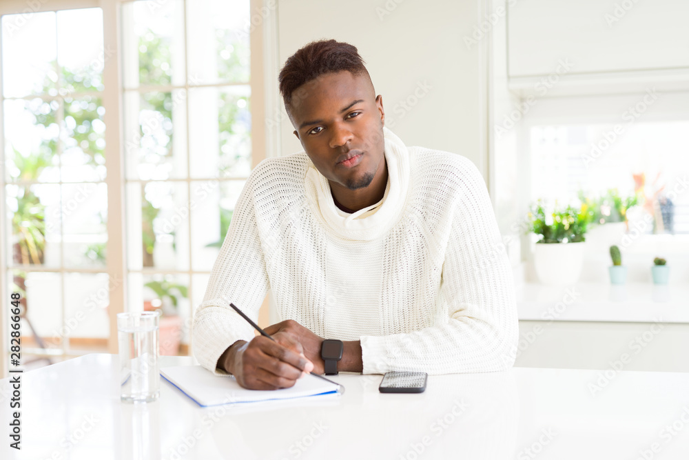 African american student man writing on a paper using a pencil with a confident expression on smart face thinking serious