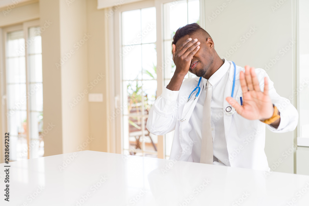 African american doctor man at the clinic covering eyes with hands and doing stop gesture with sad and fear expression. Embarrassed and negative concept. African american doctor man at the clinic covering eyes with hands and doing stop gesture with sad and fear expression. Embarrassed and negative concept.