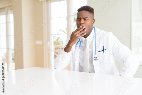 African american doctor man at the clinic bored yawning tired covering mouth with hand. Restless and sleepiness.