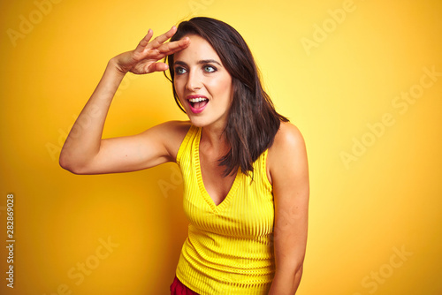 Young beautiful woman wearing t-shirt standing over yellow isolated background very happy and smiling looking far away with hand over head. Searching concept.