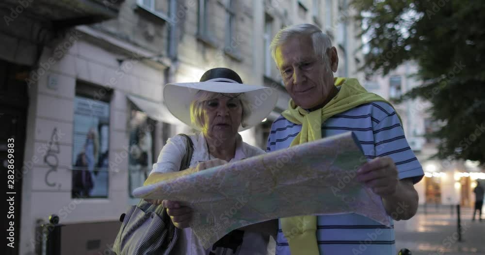 Senior male and female tourists standing with a map in hands looking for route Senior male and female tourists standing with a map in hands looking for route