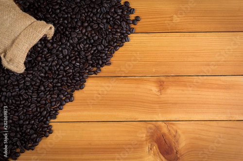 Coffee beans in a sack on wood background, top view.