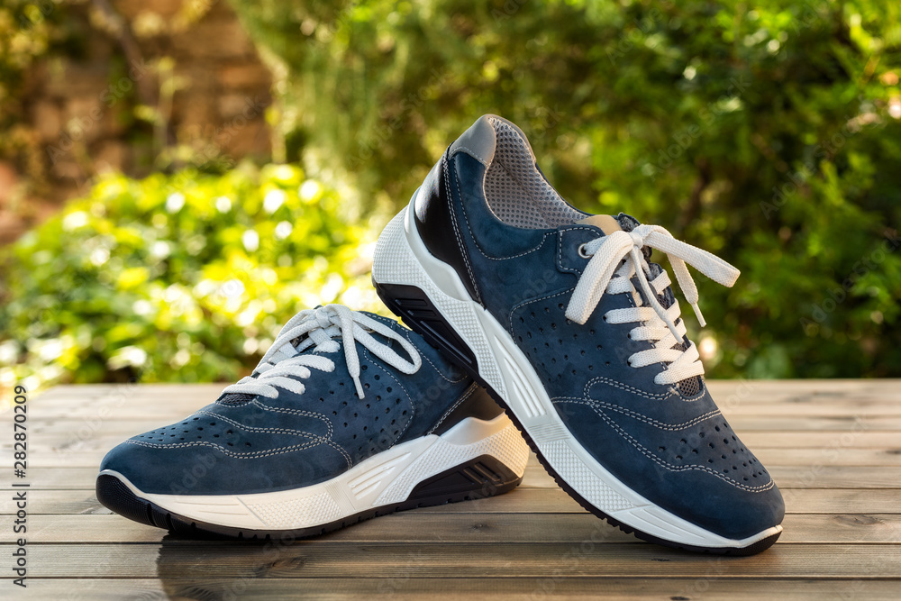 Close-up of elegant light blue sports shoes in natural nubuck leather for adult men photographed outdoors on a vintage wooden table. Fashion accessories. Close-up of elegant light blue sports shoes in natural nubuck leather for adult men photographed outdoors on a vintage wooden table. Fashion accessories.