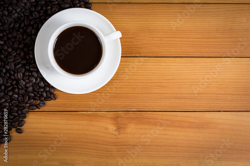 Cup of coffee and coffee beans on wood background, top view.