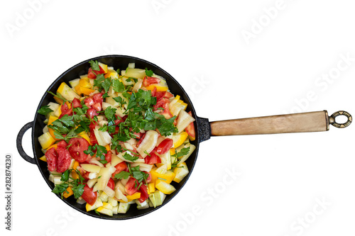 Frying pan with vegetables on a white background. Fried tomatoes, zucchini and herbs