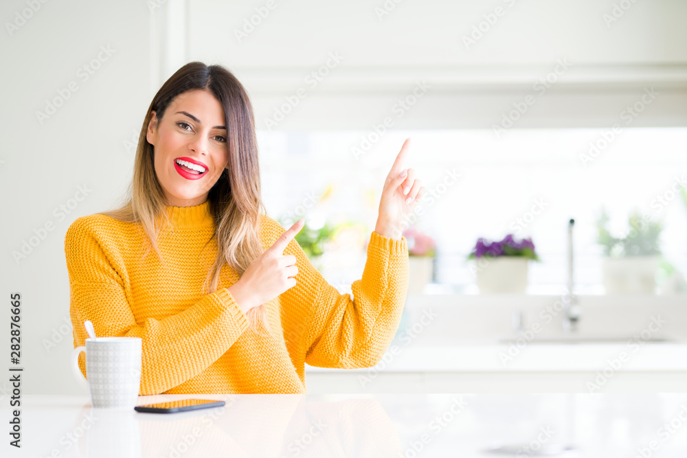 Young beautiful woman drinking a cup of coffee at home smiling and looking at the camera pointing with two hands and fingers to the side. Young beautiful woman drinking a cup of coffee at home smiling and looking at the camera pointing with two hands and fingers to the side.