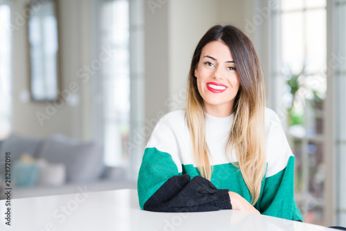 Young beautiful woman wearing winter sweater at home with a happy and cool smile on face. Lucky person.