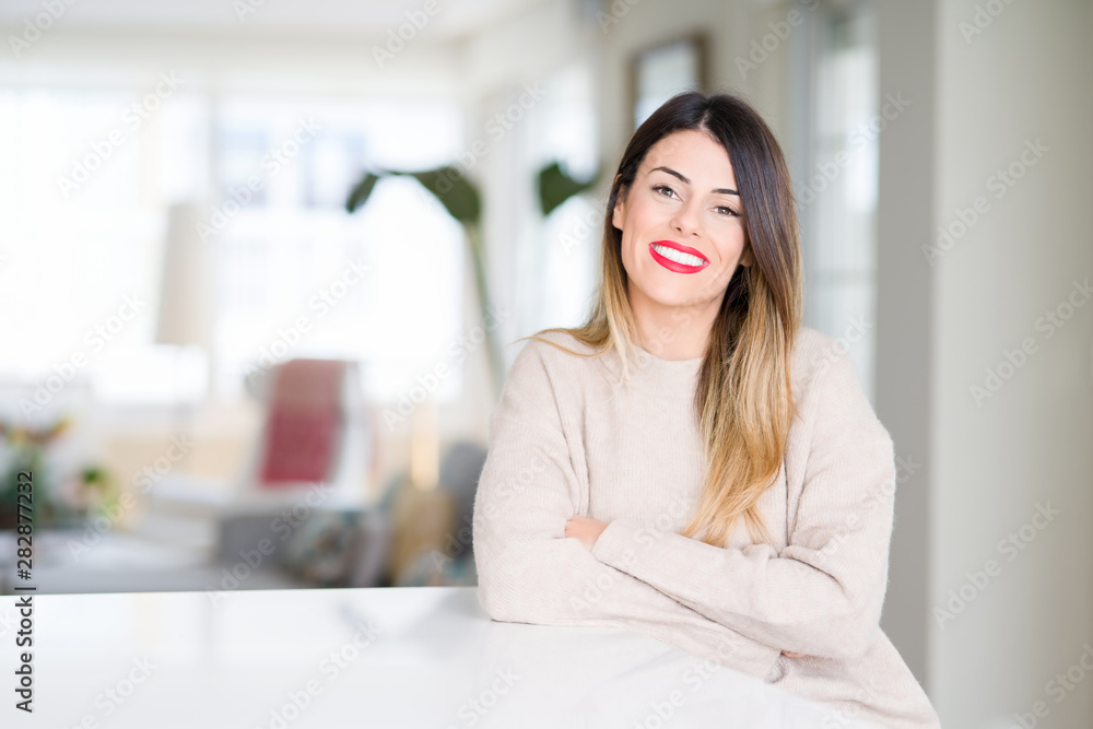 Young beautiful woman wearing winter sweater at home happy face smiling with crossed arms looking at the camera. Positive person. Young beautiful woman wearing winter sweater at home happy face smiling with crossed arms looking at the camera. Positive person.