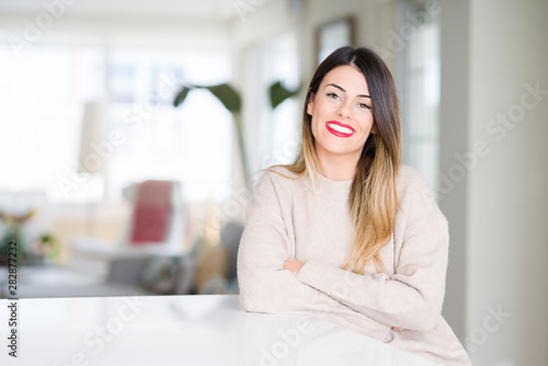 Young beautiful woman wearing winter sweater at home happy face smiling with crossed arms looking at the camera. Positive person.