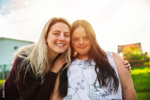 A Portrait of trisomie 21 adult girl smilin outside at sunset with family friend photo