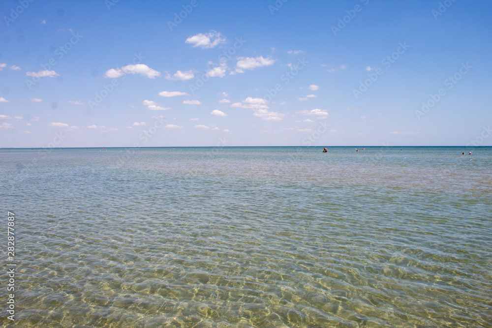 Summer beautiful seascape - transparent sea with a sandy bottom and blue sky, summer breeze.
