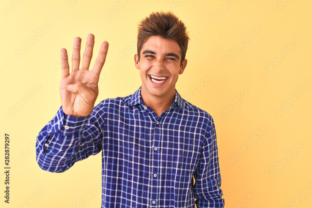 Young handsome man wearing casual shirt standing over isolated yellow background showing and pointing up with fingers number four while smiling confident and happy. Young handsome man wearing casual shirt standing over isolated yellow background showing and pointing up with fingers number four while smiling confident and happy.