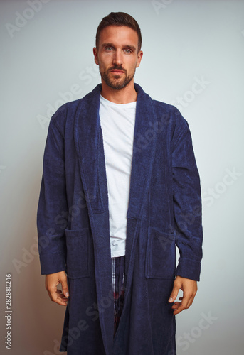 Young man wearing comfortable pajamas and robe at morning over isolated background with serious expression on face. Simple and natural looking at the camera.