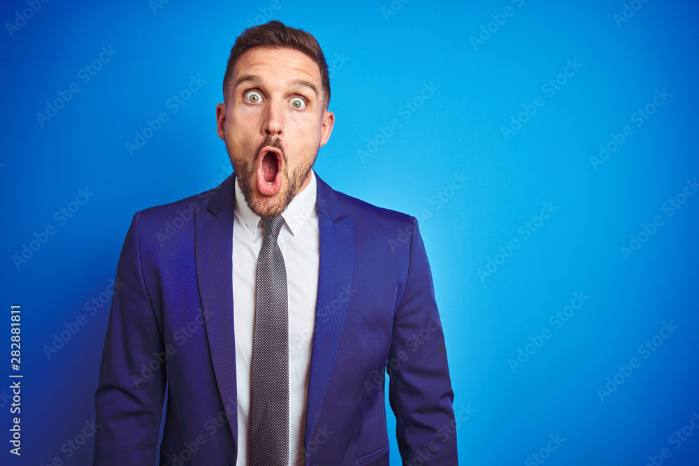 Young handsome business man over blue isolated background afraid and shocked with surprise expression, fear and excited face. Young handsome business man over blue isolated background afraid and shocked with surprise expression, fear and excited face.