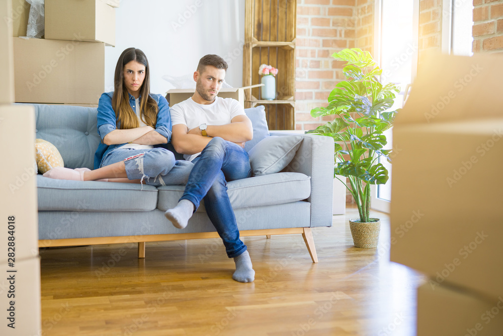 Young beautiful couple relaxing sitting on the sofa around boxes from moving to new house skeptic and nervous, disapproving expression on face with crossed arms. Negative person. Young beautiful couple relaxing sitting on the sofa around boxes from moving to new house skeptic and nervous, disapproving expression on face with crossed arms. Negative person.