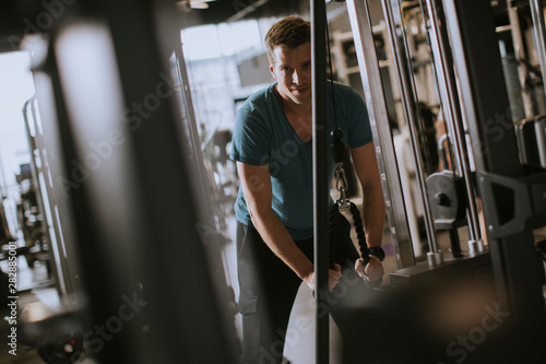Young sporty man working out on pull-down machine in gym