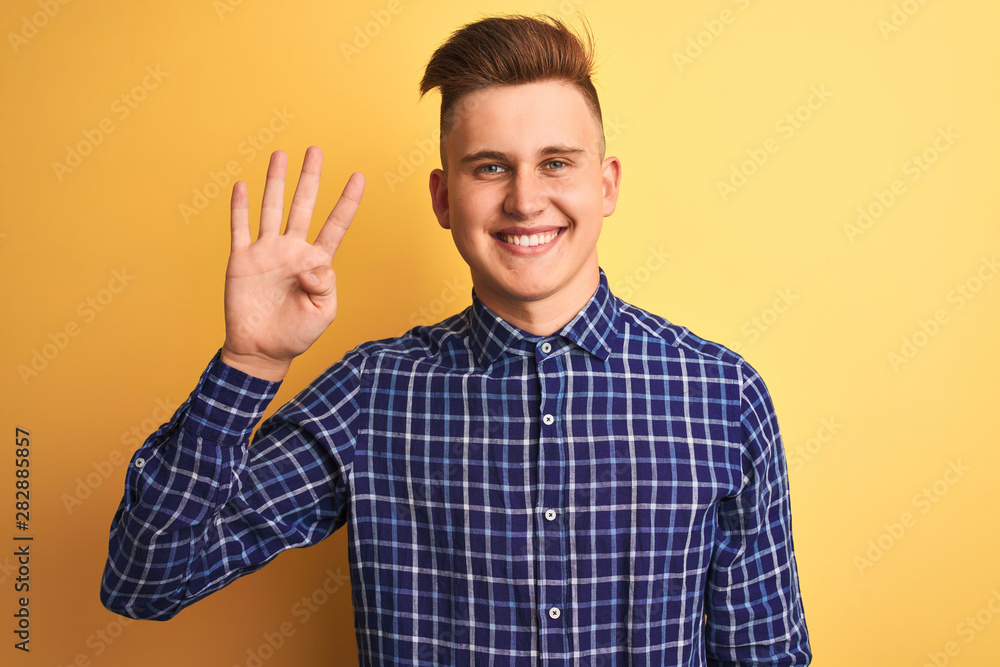 Young handsome man wearing casual shirt standing over isolated yellow background showing and pointing up with fingers number four while smiling confident and happy. Young handsome man wearing casual shirt standing over isolated yellow background showing and pointing up with fingers number four while smiling confident and happy.