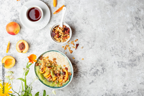 Bowl of fresh oatmeal porridge with kiwi, peach and granola