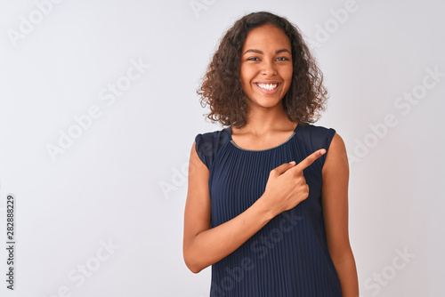 Young brazilian woman wearing blue dress standing over isolated white background cheerful with a smile of face pointing with hand and finger up to the side with happy and natural expression on face