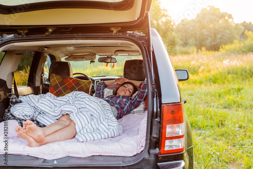 woman sleeps comfortably her car Luggage compartment nature summer under blanket. concept caravanning free travel for weekend. photo