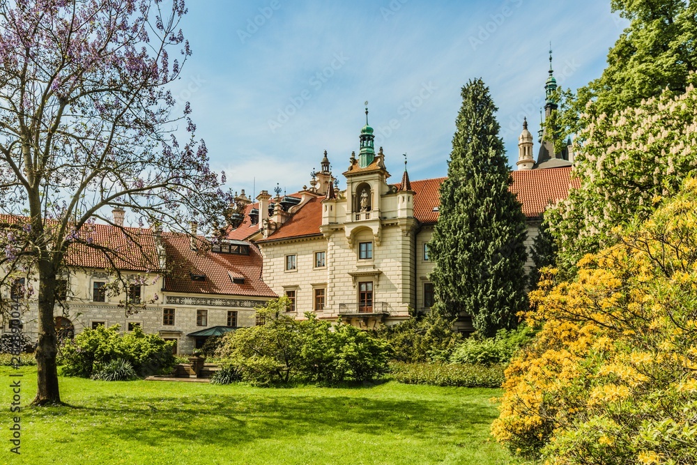 Pruhonice / Czech Republic - May 19 2019: Spring view of romantic castle standing in a garden with green grass, trees and colorful blossoms. Sunny day with blue sky.