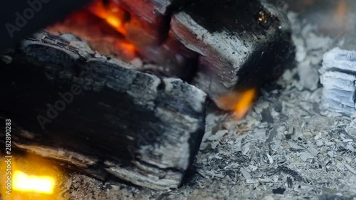 burning black coals close-up. The wind blows away flakes of gray ash and smoke. The edge of the wood burns with a small flame.