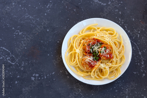 Spaghetti with meatballs, tomato sauce and parmesan cheese in white plate on dark background