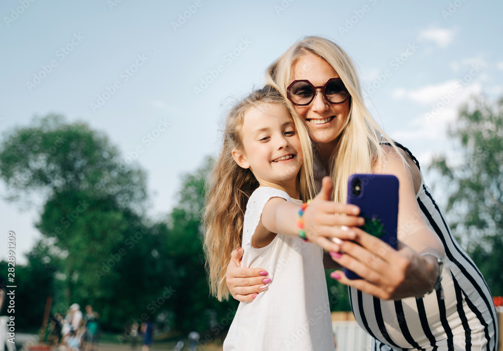 Image of happy mother and daughter taking selfie on street on summer day Image of happy mother and daughter taking selfie on street on summer day