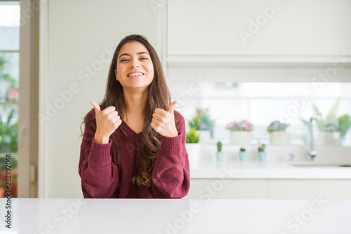 Young beautiful woman at home success sign doing positive gesture with hand, thumbs up smiling and happy. Looking at the camera with cheerful expression, winner gesture.