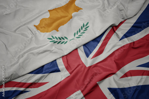 waving colorful flag of great britain and national flag of cyprus.