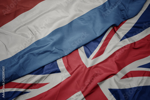 waving colorful flag of great britain and national flag of luxembourg.