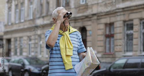 Senior tourist exploring town with a map. Looking in binoculars