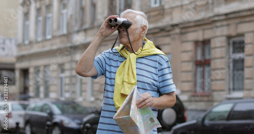 Senior tourist exploring town with a map. Looking in binoculars