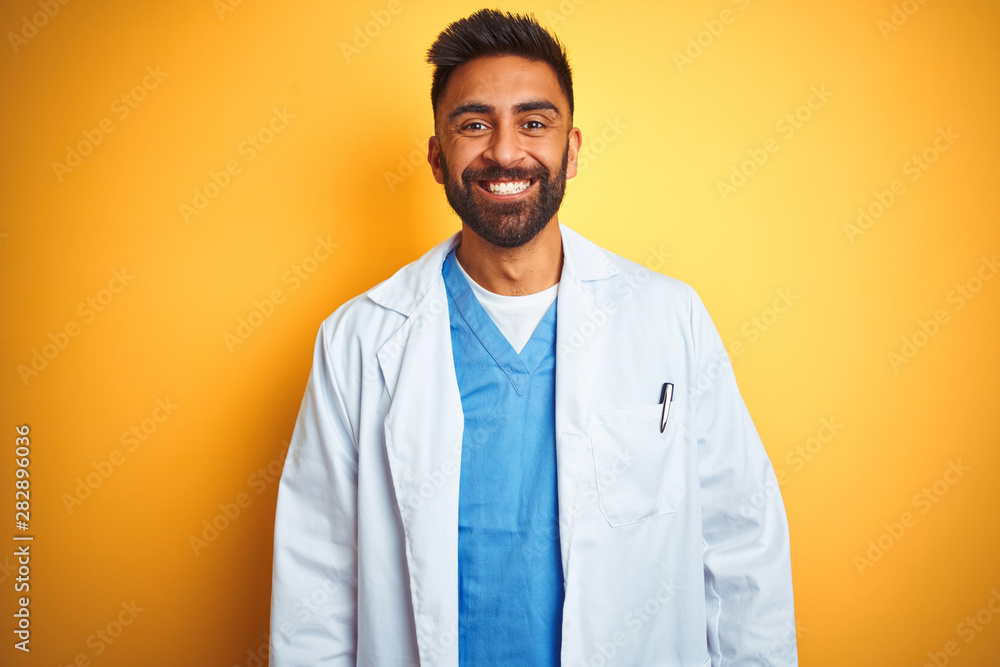 Young indian doctor man standing over isolated yellow background with a happy and cool smile on face. Lucky person. - obrazy, fototapety, plakaty 