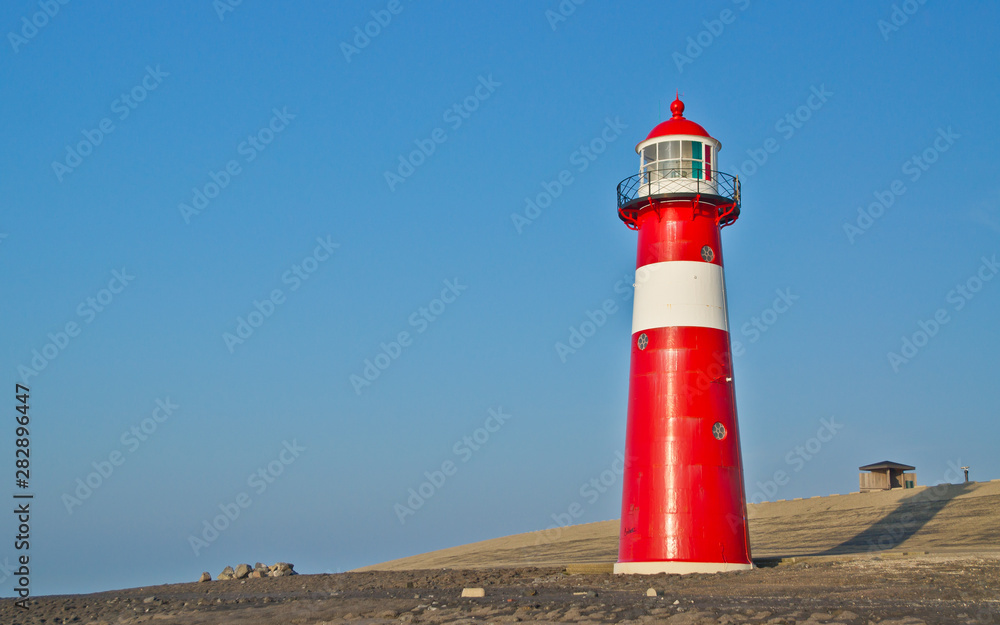 Red-white lighthouse in front of the North Sea dike.