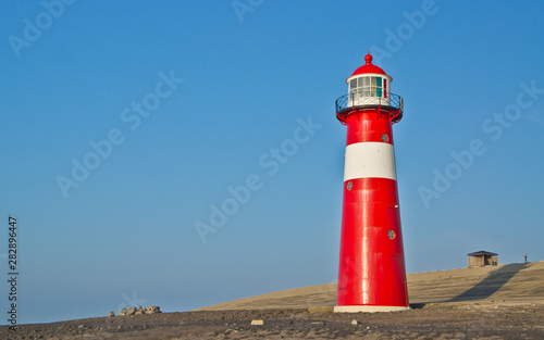 Red-white lighthouse in front of the North Sea dike.