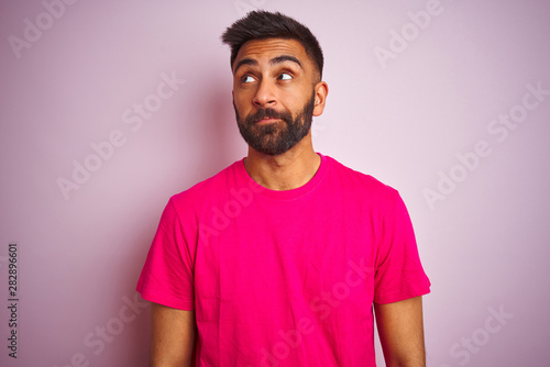 Young indian man wearing t-shirt standing over isolated pink background smiling looking to the side and staring away thinking.