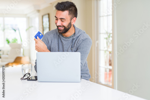 Handsome man smiling using credit card as payment metod when shopping online using laptop photo