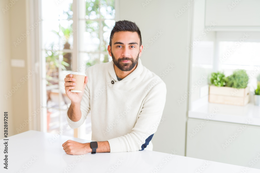 Handsome hispanic man drinking a coffee in a paper cup with a confident expression on smart face thinking serious