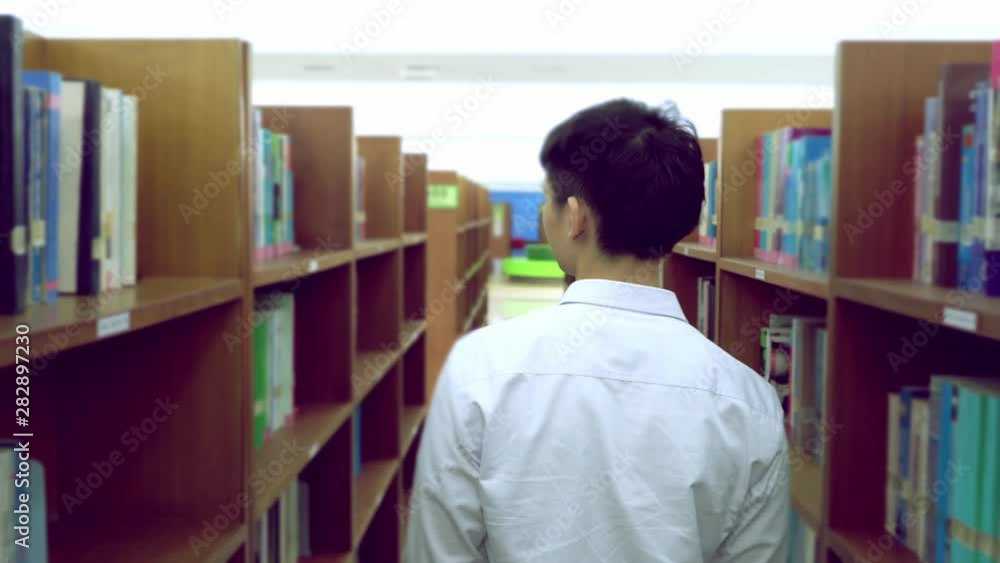 Young asian is walking between book shelf,choose books in the library,Concept educational. Young asian is walking between book shelf,choose books in the library,Concept educational.